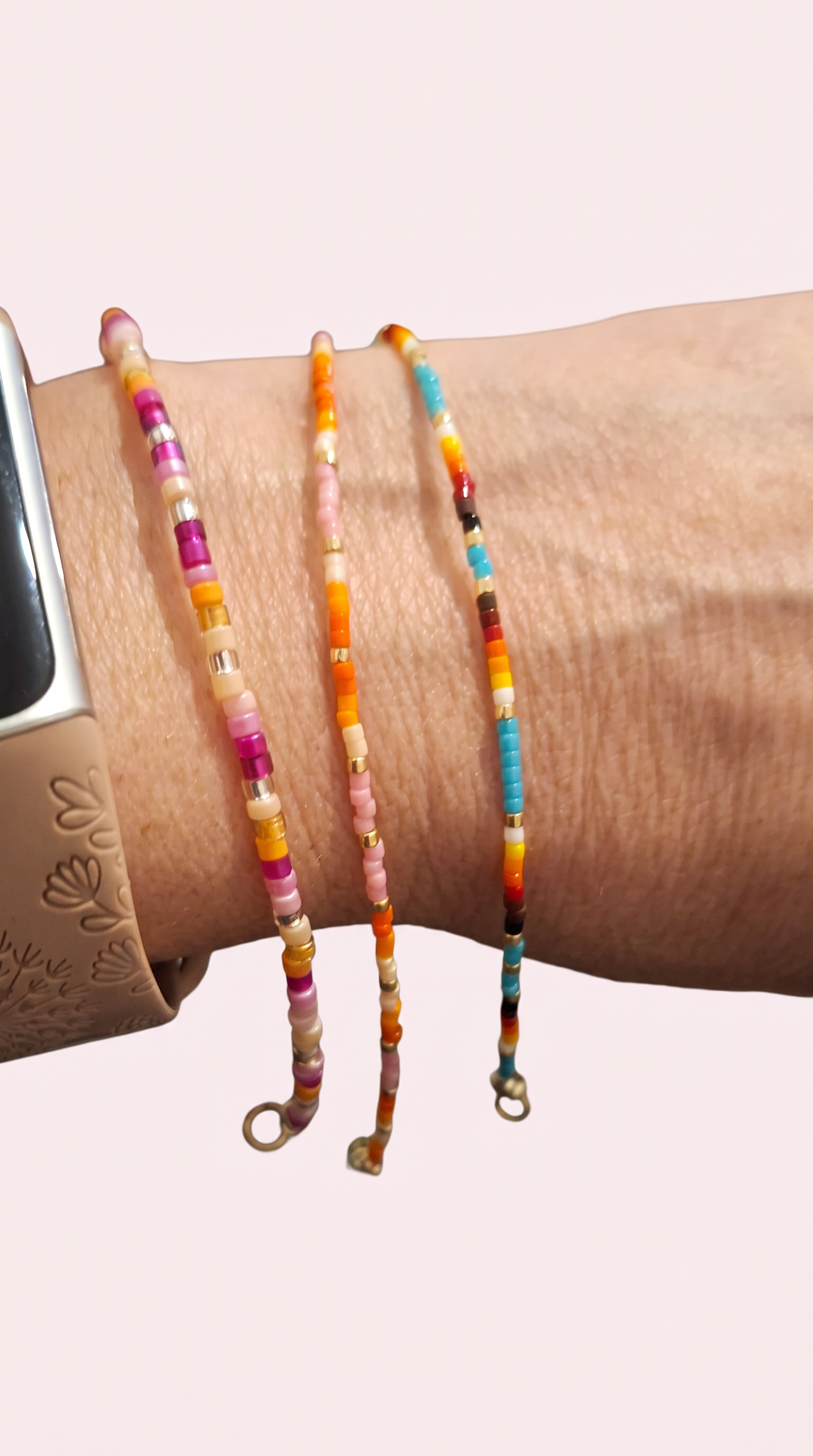 Three thin bracelets on a wrist, with pink and burgundy, orange and peach, and rainbow bead bands